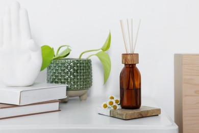 Photo of Aromatic reed air freshener, chamomiles and houseplant on white table