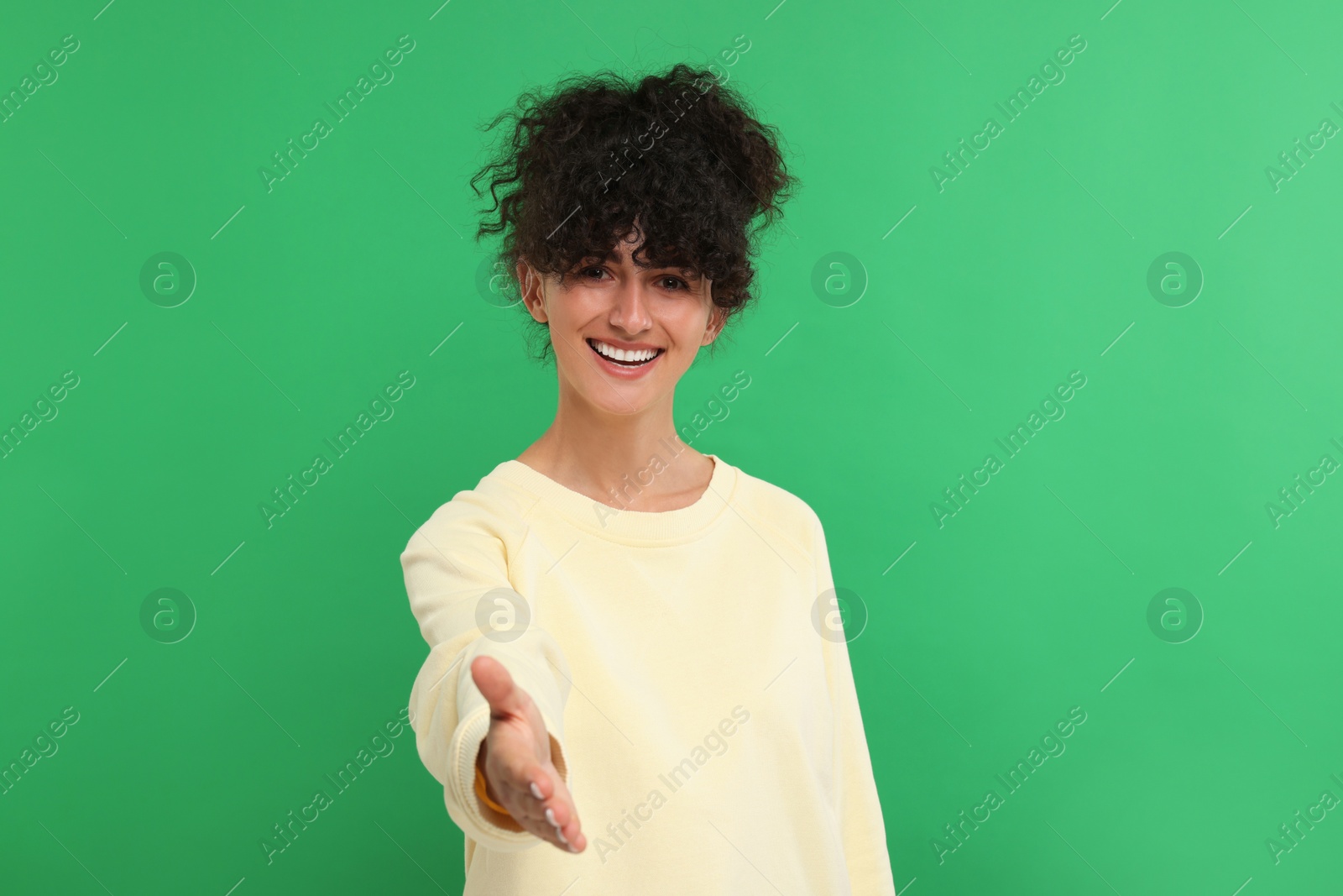 Photo of Happy young woman welcoming and offering handshake on green background