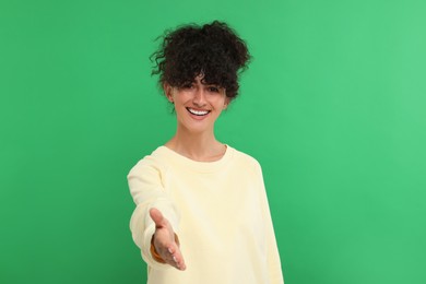 Photo of Happy young woman welcoming and offering handshake on green background