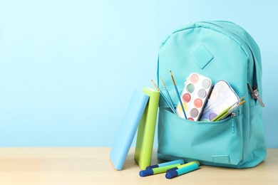 Photo of Stylish backpack and different school stationery on wooden table against light blue background, space for text. Back to school