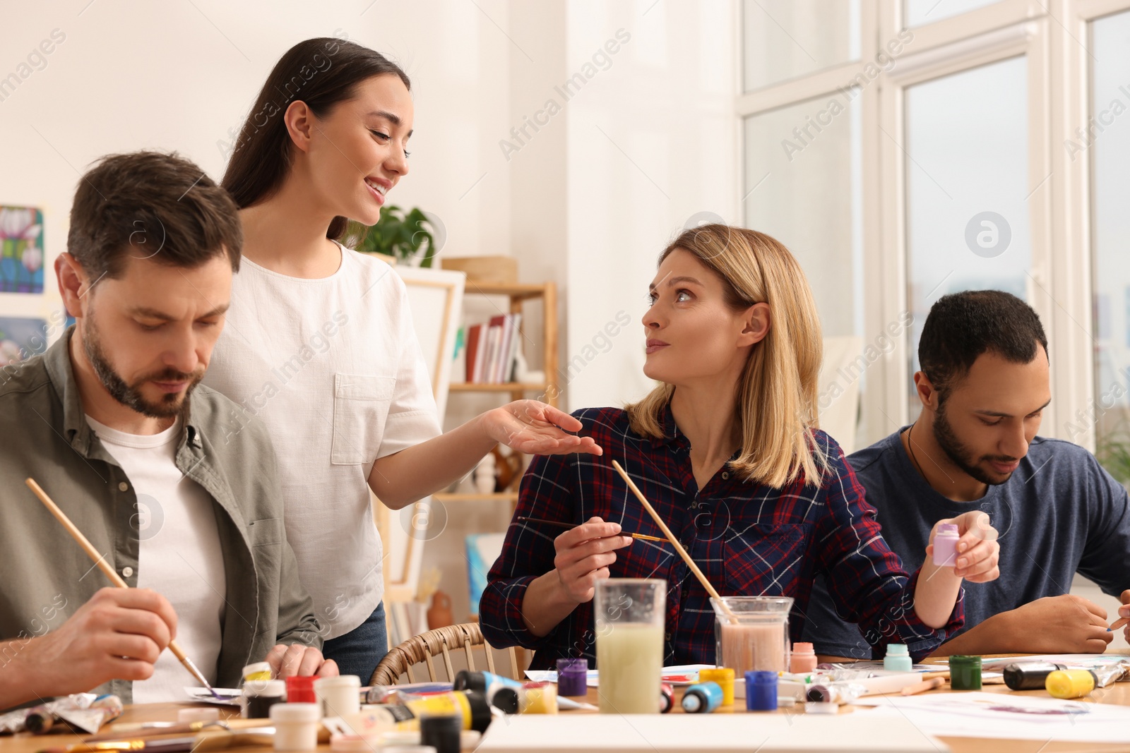 Photo of Artist teaching her students to paint at table in studio. Creative hobby