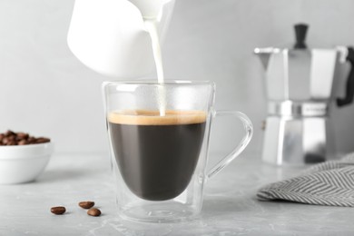 Photo of Pouring milk into cup with aromatic coffee on grey marble table