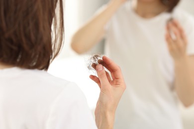 Photo of Woman holding clump of lost hair near mirror indoors, closeup. Alopecia problem