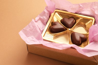 Photo of Partially empty box of chocolate candies on light brown background, closeup. Space for text