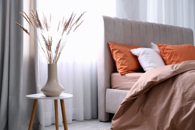 Photo of Vase with decorative dried plants on table in bedroom. Interior design