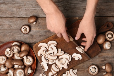 Young woman cutting fresh champignon mushrooms on wooden board, top view