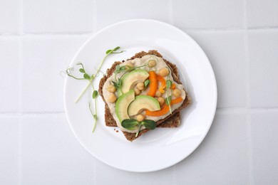 Tasty vegan sandwich with avocado, chickpeas and bell pepper on white tiled table, top view