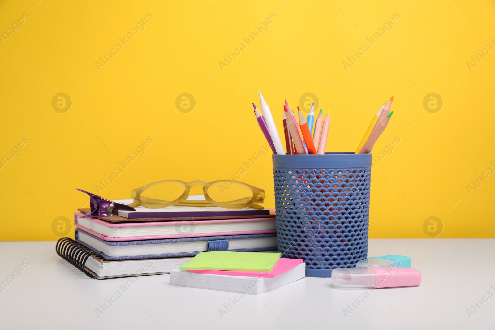 Photo of Different school stationery and glasses on white table against yellow background. Back to school