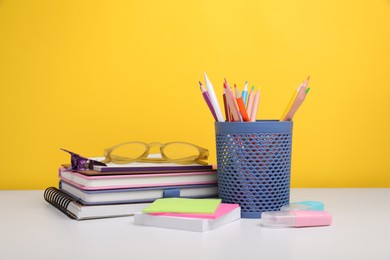 Different school stationery and glasses on white table against yellow background. Back to school