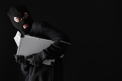 Photo of Thief in balaclava with briefcase of money on black background. Space for text