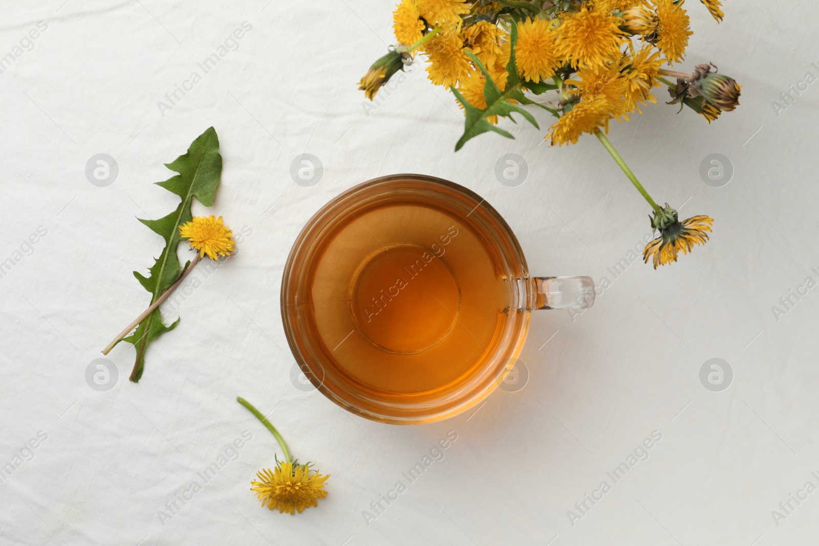 Photo of Delicious fresh tea and dandelion flowers on white table, flat lay