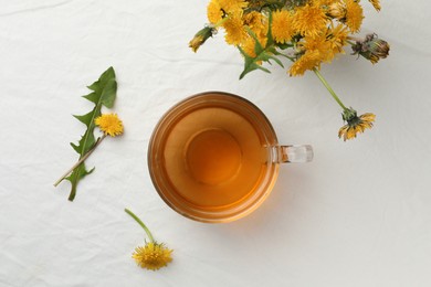 Delicious fresh tea and dandelion flowers on white table, flat lay