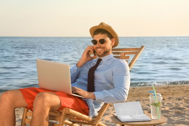 Man with laptop talking by mobile phone on beach. Business trip