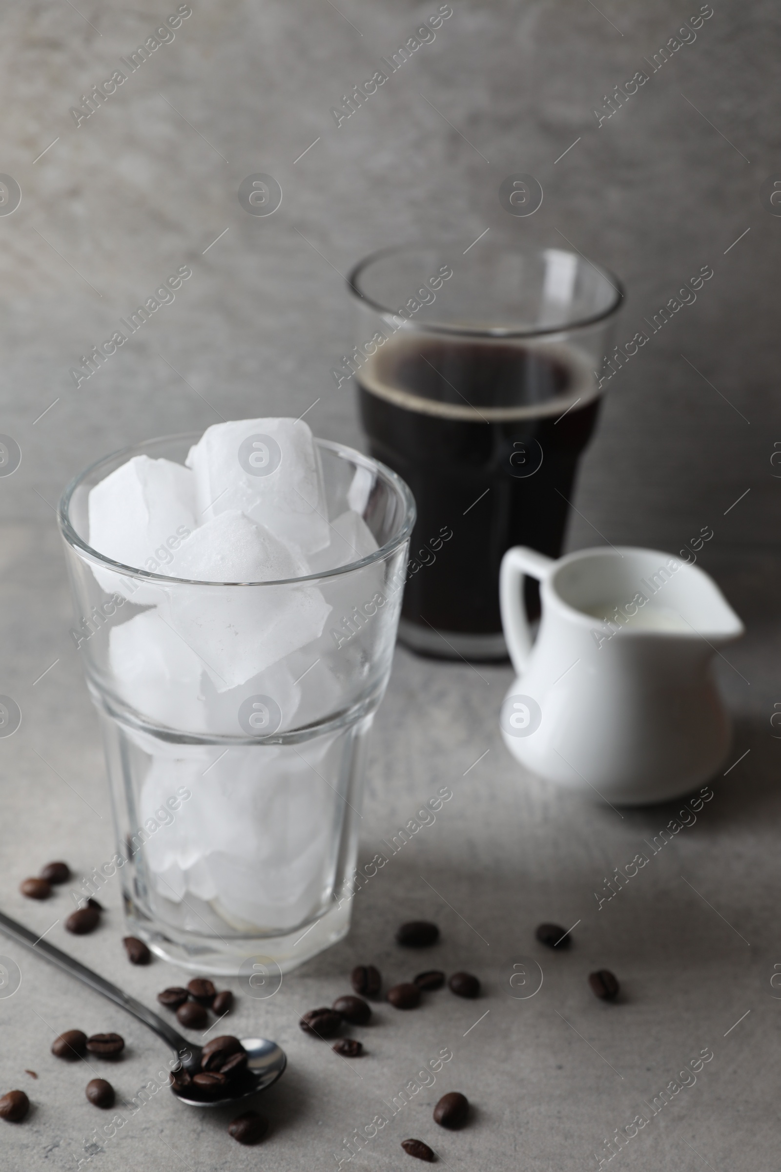 Photo of Making iced coffee. Ice cubes in glass, ingredients and spoon on gray table