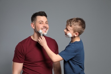 Son applying shaving foam on dad's face, grey background