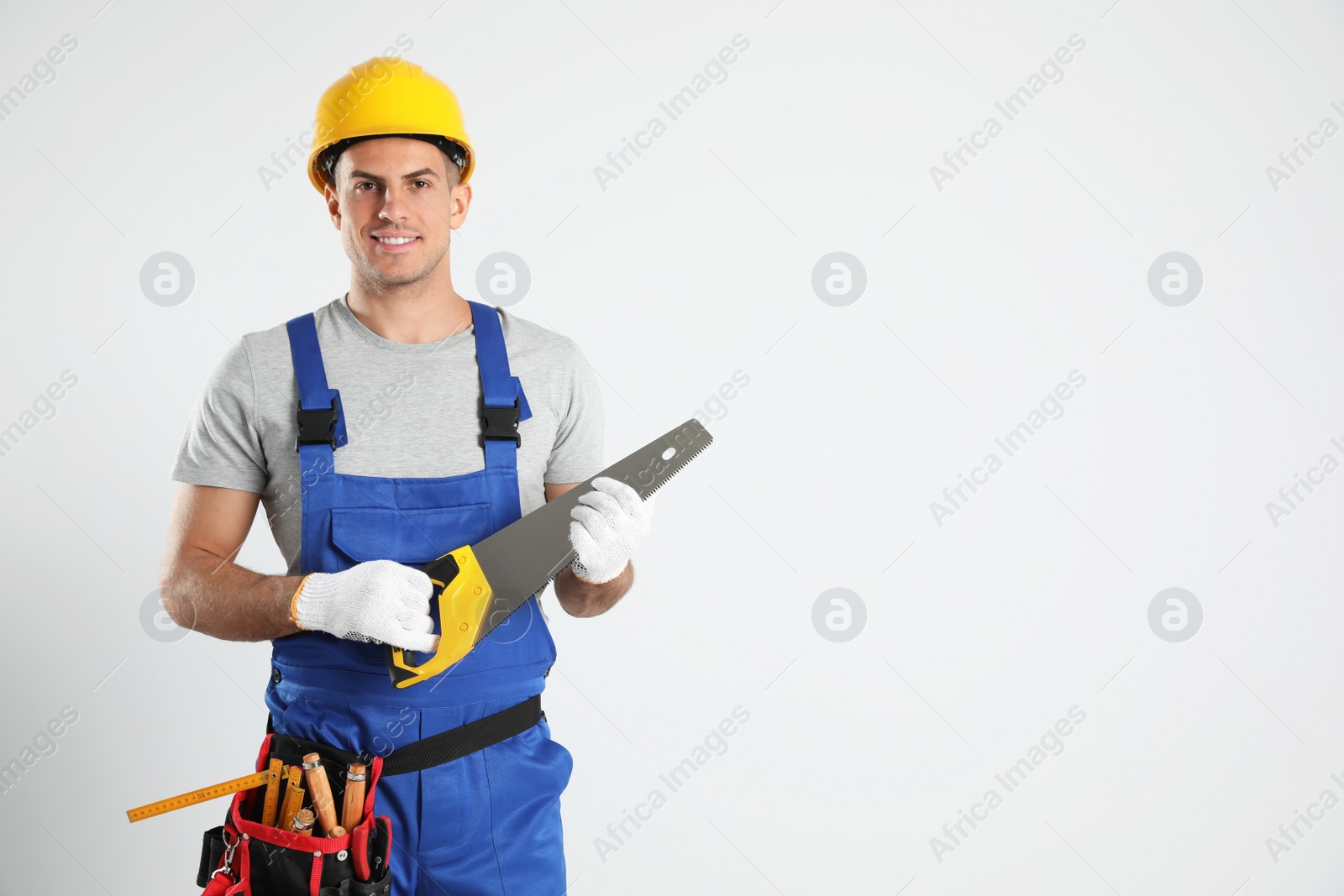 Photo of Carpenter with tool belt and hand saw on light background. Space for text