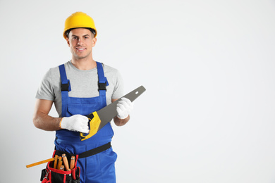 Photo of Carpenter with tool belt and hand saw on light background. Space for text