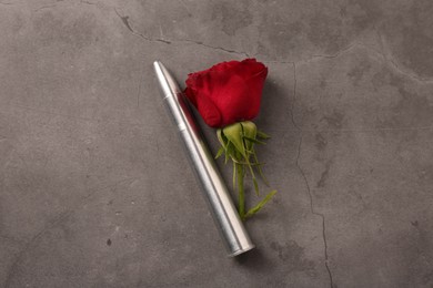 Metal bullet and beautiful rose on grey textured table, flat lay