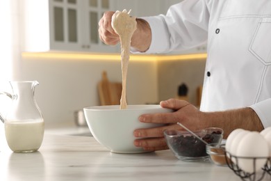 Photo of Professional chef making dough at white marble table indoors, closeup