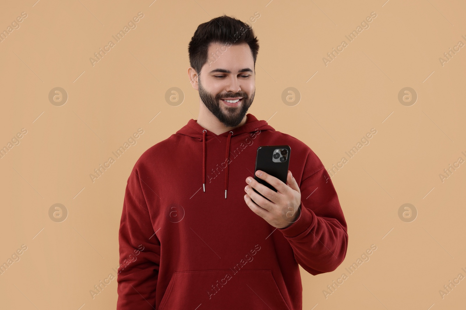 Photo of Happy young man using smartphone on beige background