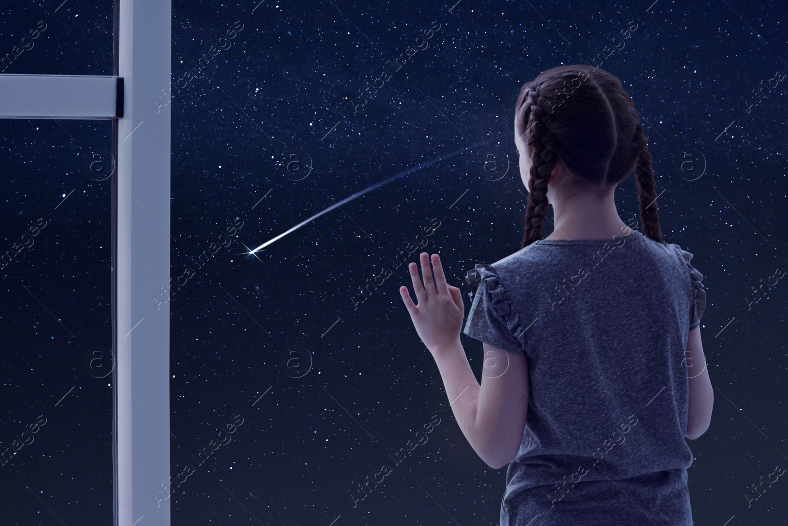Image of Little girl near window looking at shooting star in beautiful night sky