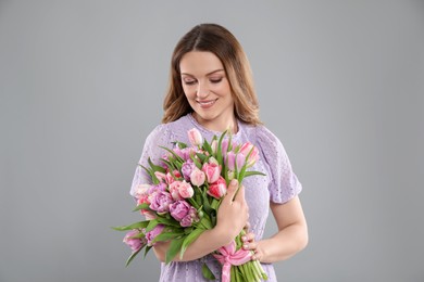 Happy young woman with bouquet of beautiful tulips on grey background