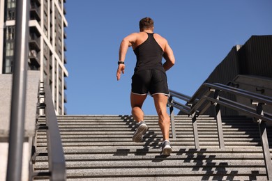 Photo of Man running up stairs outdoors on sunny day, back view