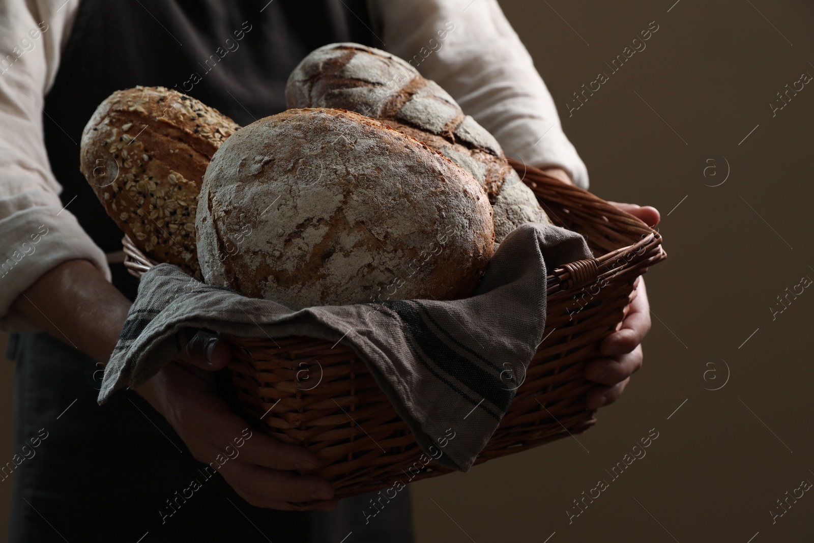 Photo of Man holding wicker basket with different types of bread on brown background, closeup