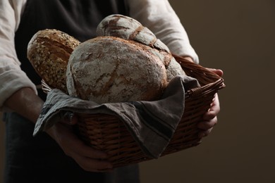 Photo of Man holding wicker basket with different types of bread on brown background, closeup