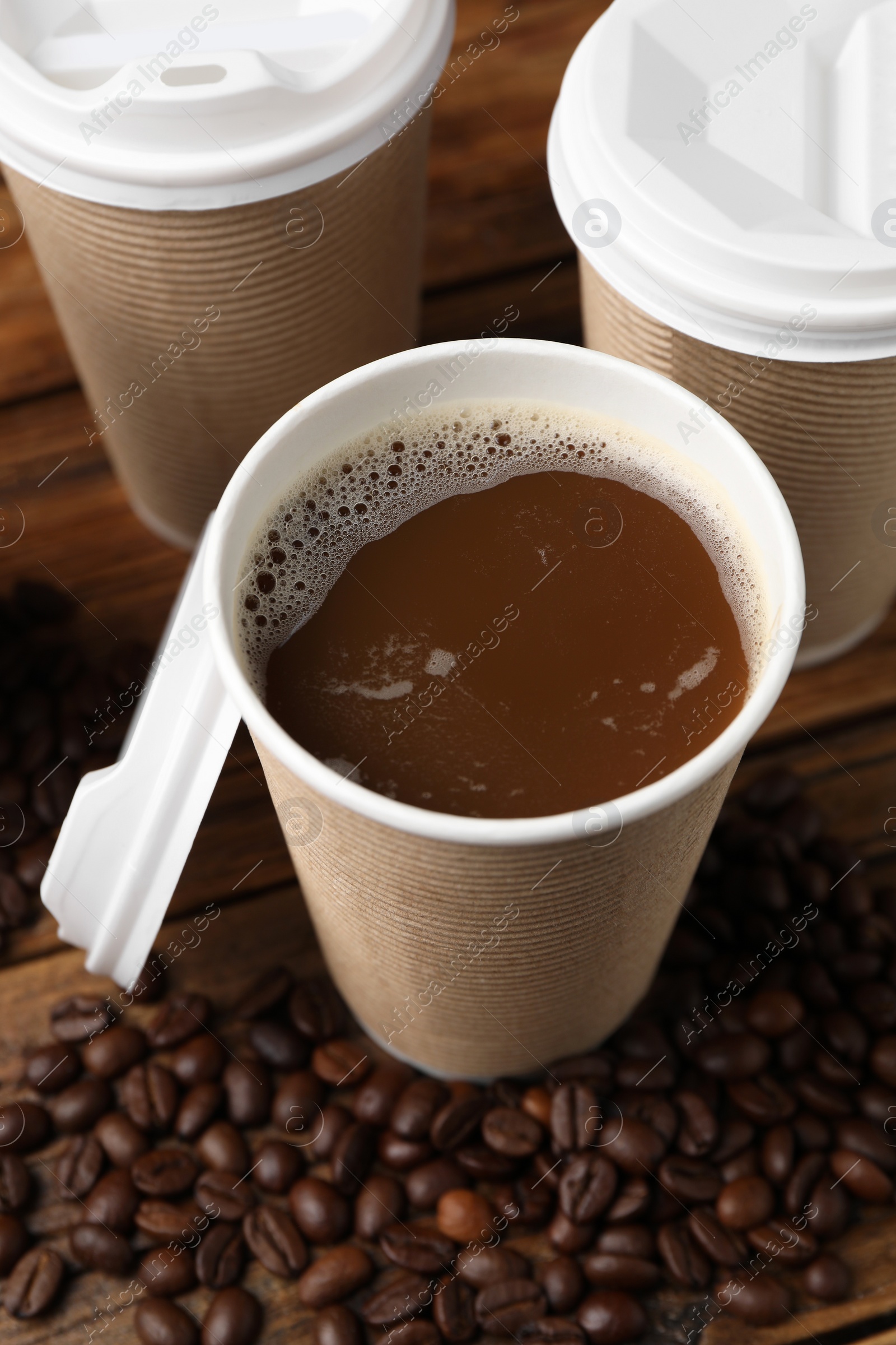 Photo of Coffee to go. Paper cups with tasty drink and beans on wooden table, closeup