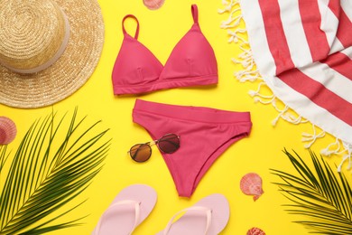 Photo of Towel, swimsuit and different beach accessories on yellow background, flat lay