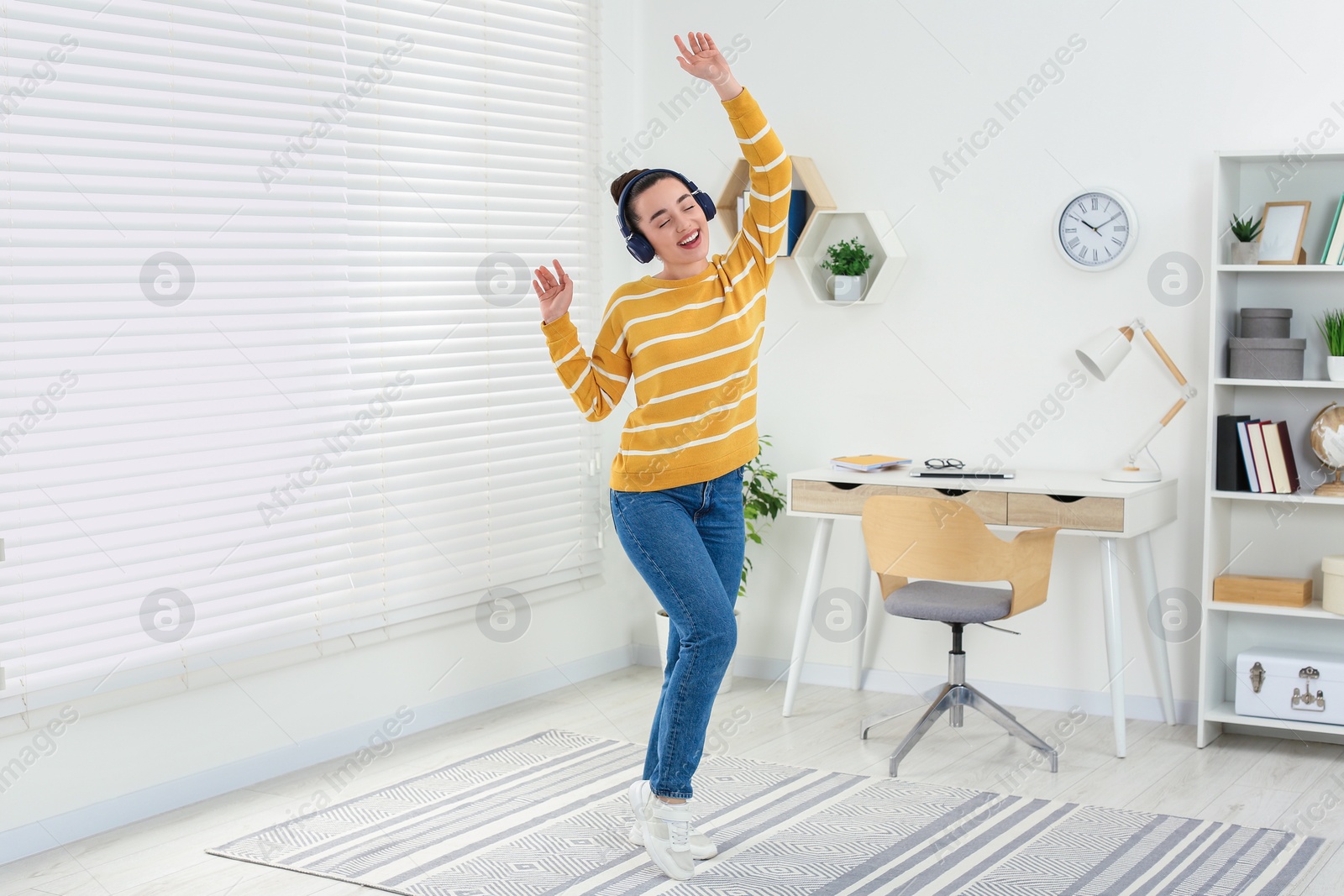 Photo of Happy woman in headphones listening music and dancing in cosy room