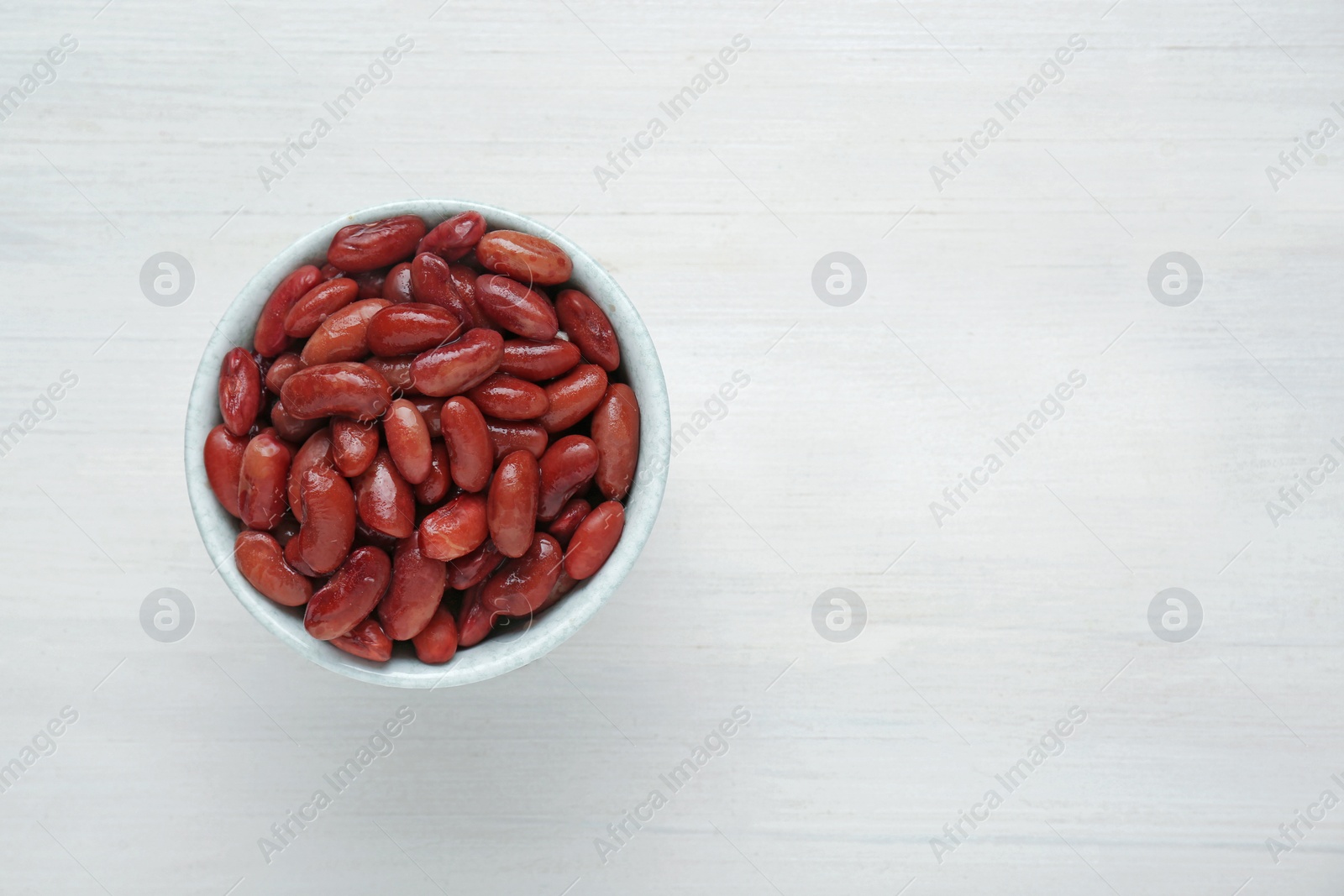 Photo of Bowl of canned kidney beans on white wooden table, top view. Space for text