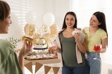 Happy pregnant woman and her friends with tasty treats at baby shower party