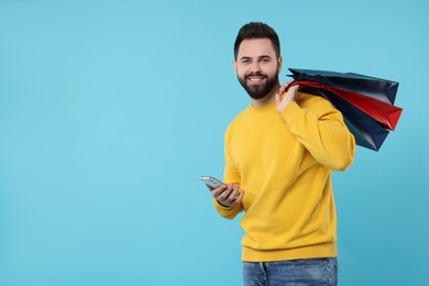 Smiling man with paper shopping bags and smartphone on light blue background. Space for text
