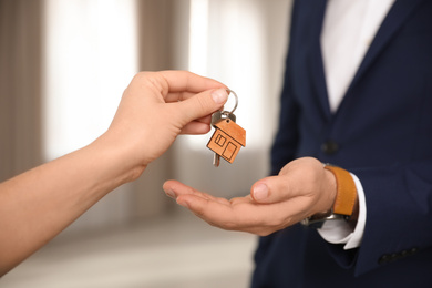 Photo of Real estate agent giving key with trinket to client in office, closeup