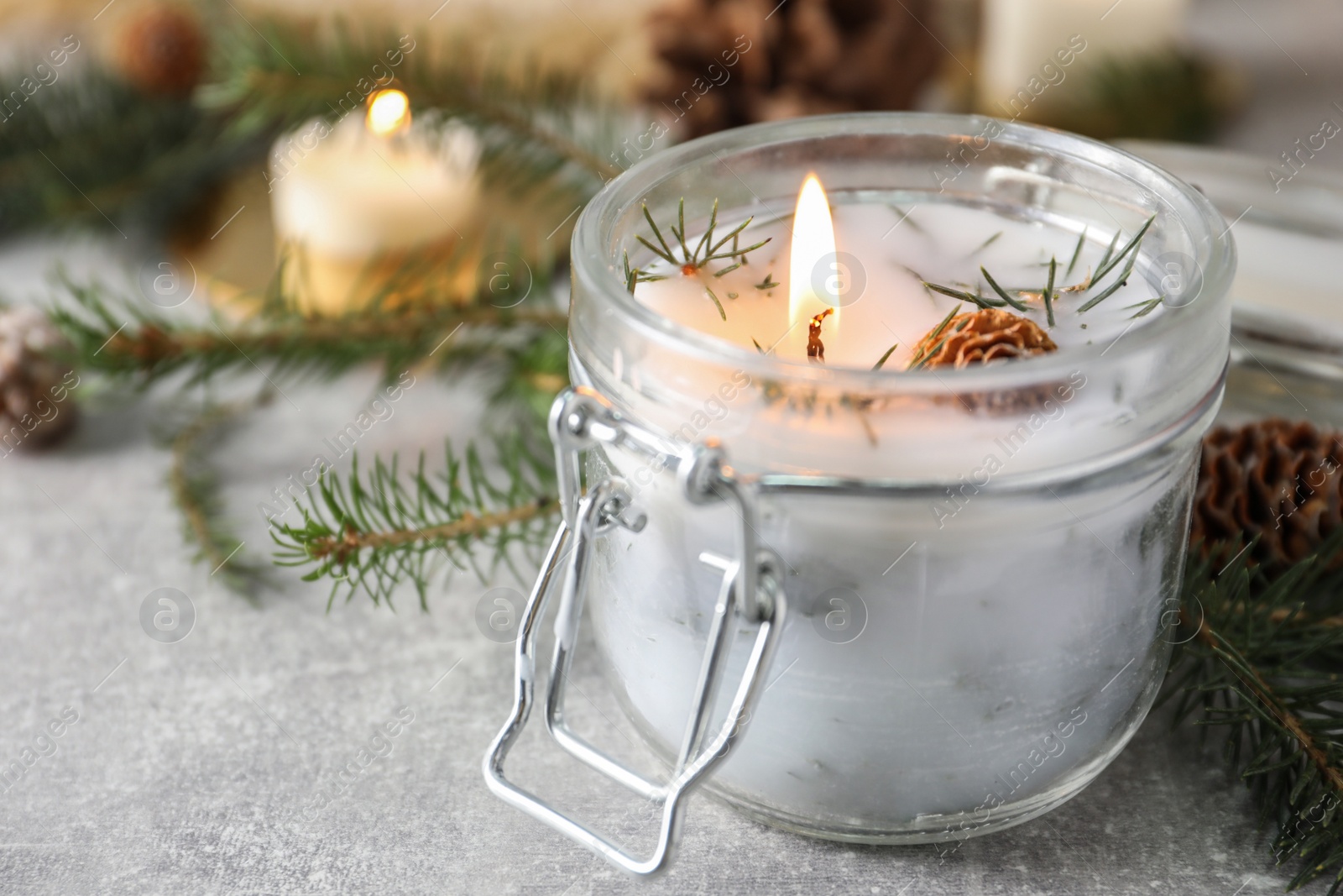 Photo of Burning scented conifer candle and Christmas decor on grey table, closeup. Space for text