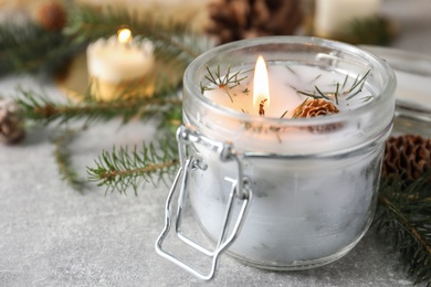 Burning scented conifer candle and Christmas decor on grey table, closeup. Space for text