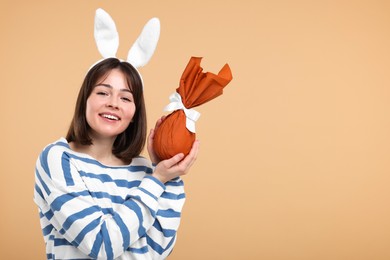 Photo of Easter celebration. Happy woman with bunny ears and wrapped egg on beige background, space for text