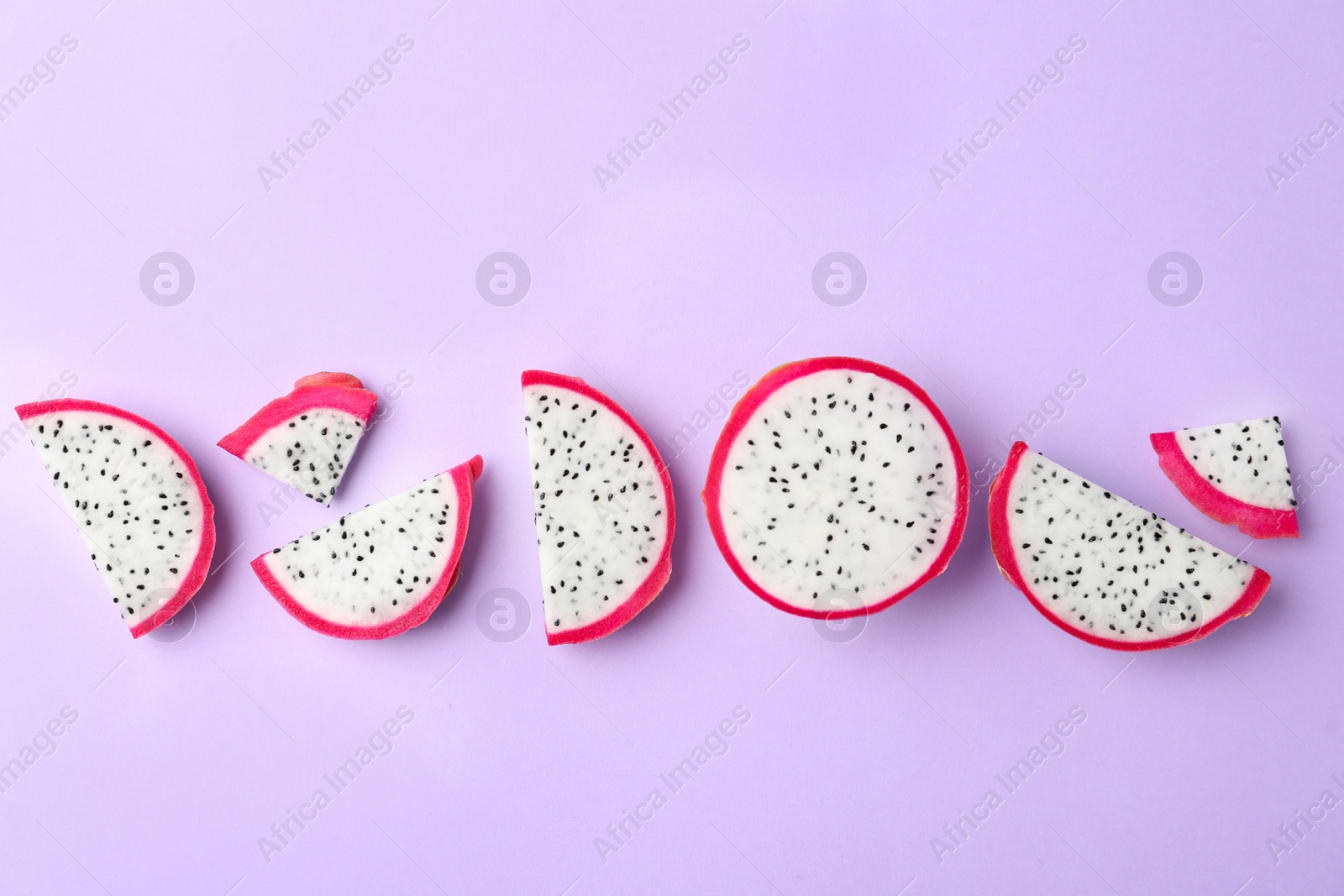 Photo of Slices of delicious dragon fruit (pitahaya) on violet background, flat lay