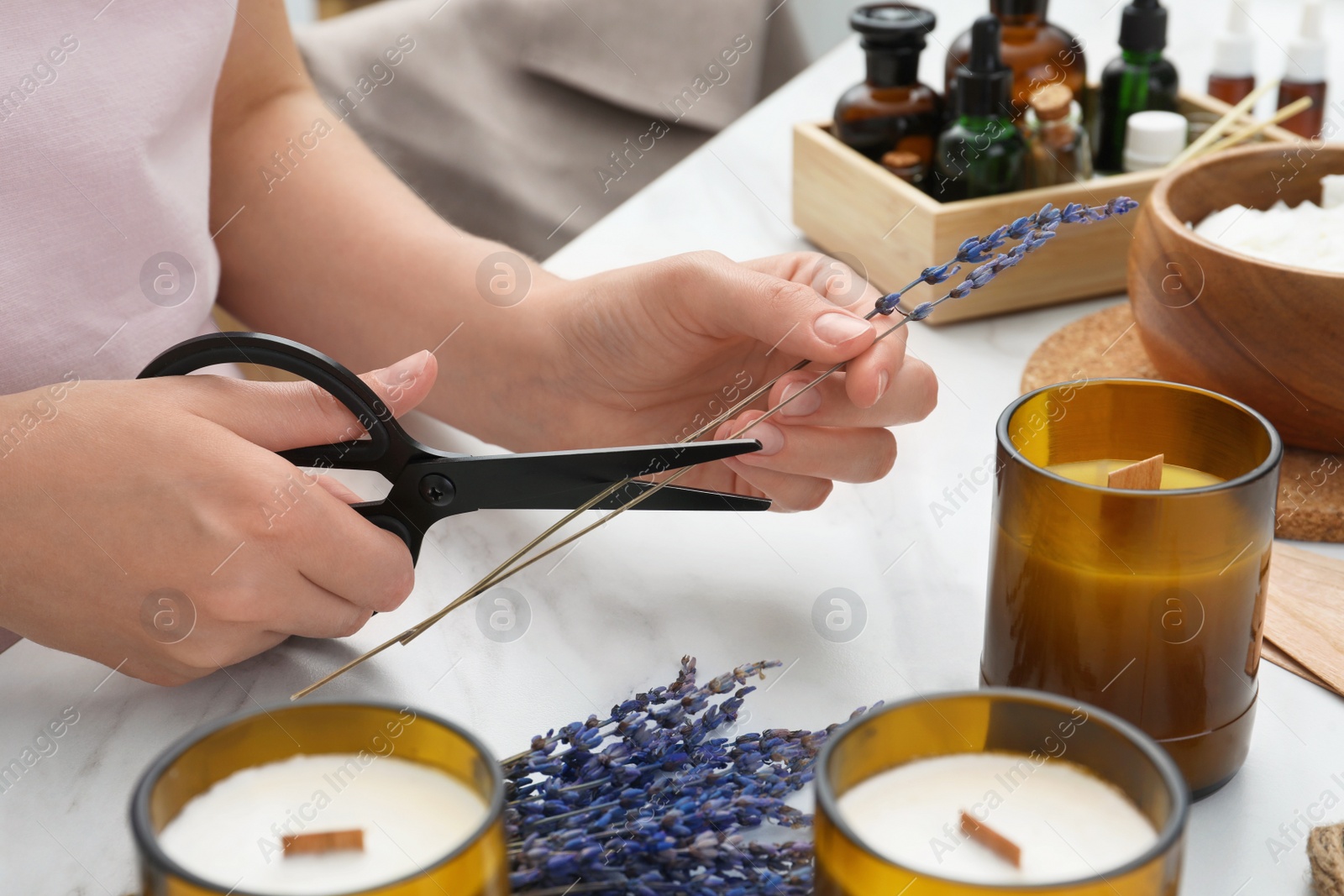 Photo of Woman decorating homemade candle with lavender flowers at table indoors, closeup