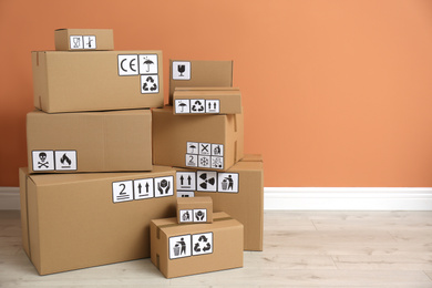 Photo of Cardboard boxes with different packaging symbols on floor near orange wall, space for text. Parcel delivery