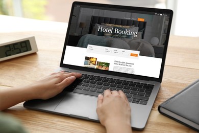 Woman using laptop to book hotel at wooden table, closeup