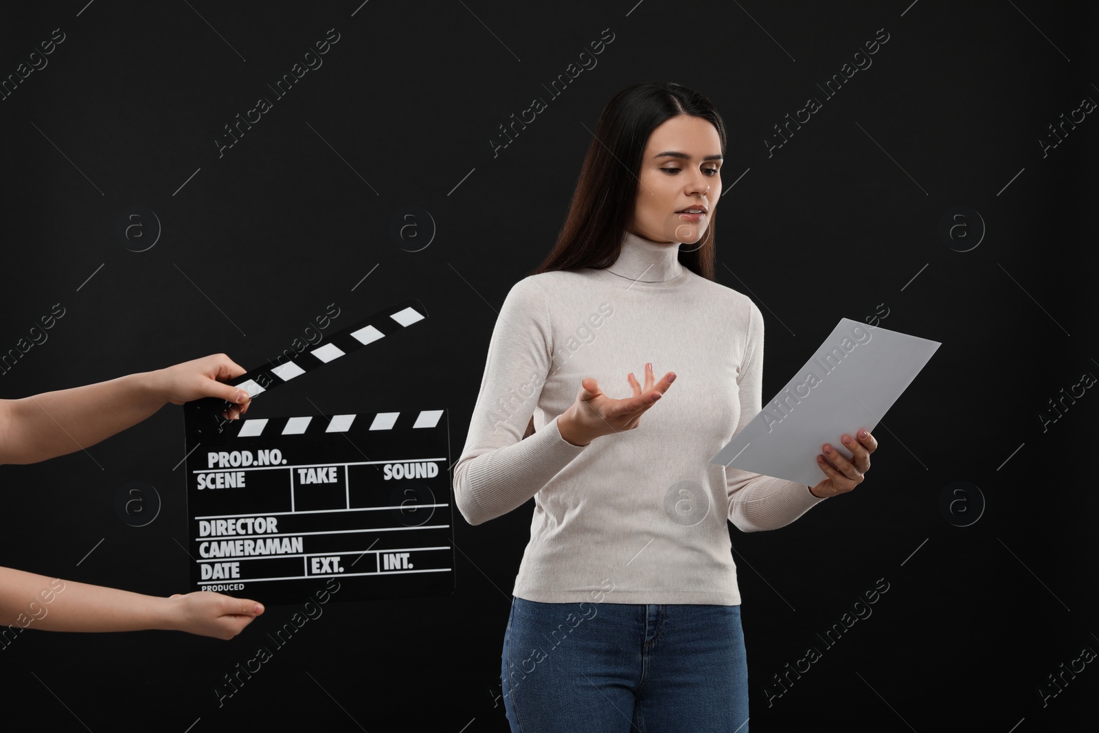 Photo of Actress performing while second assistant camera holding clapperboard on black background. Film industry