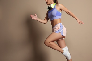 Young woman in sportswear with headphones running on beige background, closeup