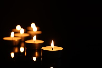 Photo of Burning candles on mirror surface in darkness, closeup. Space for text