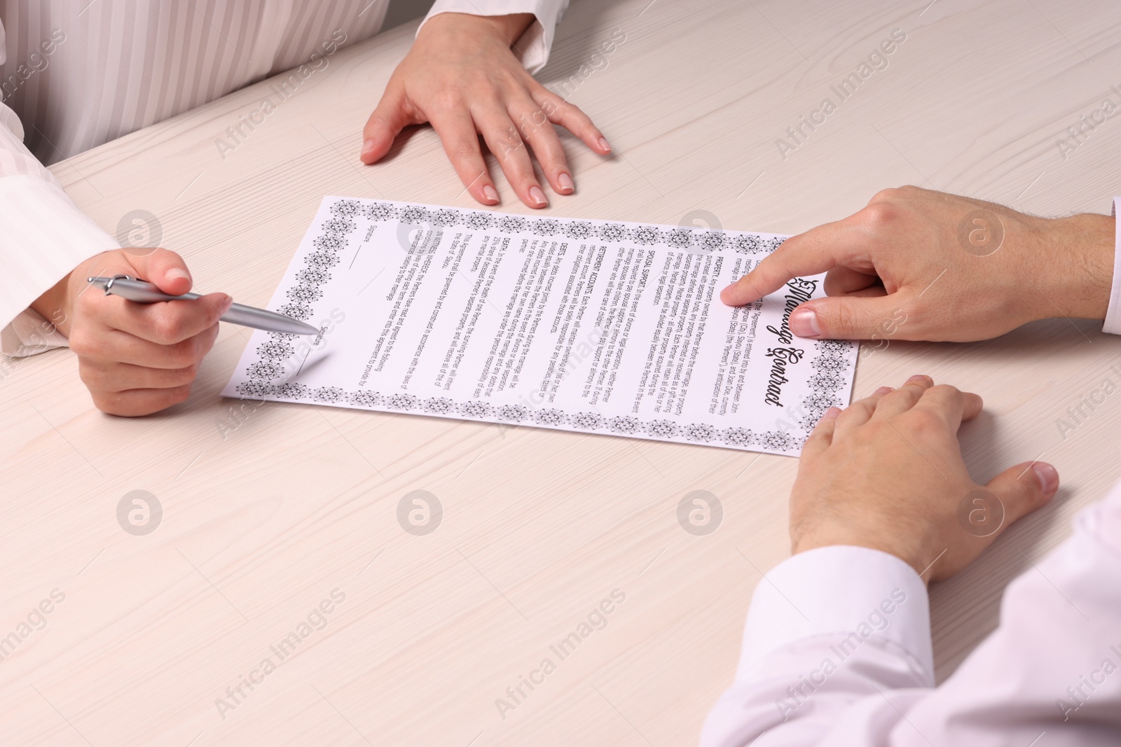 Photo of Man and woman signing marriage contract at light wooden table, closeup