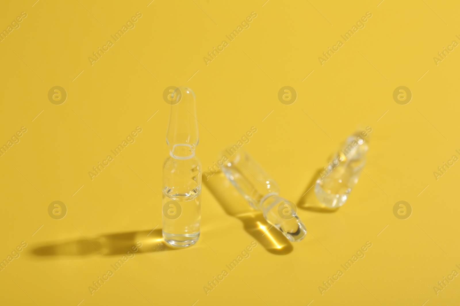 Photo of Glass ampoules with liquid on yellow background