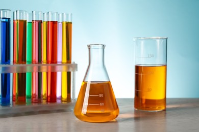 Different laboratory glassware with colorful liquids on wooden table against turquoise background