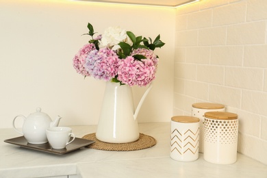 Photo of Beautiful bouquet of hydrangea flowers and tea on light countertop